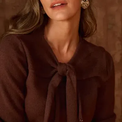 Mulher com camisola castanha de malha com laço e brincos dourados
