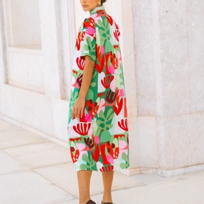 Vestido midi colorido com padrão abstrato em verde, vermelho, rosa e branco num cenário de pedra clara