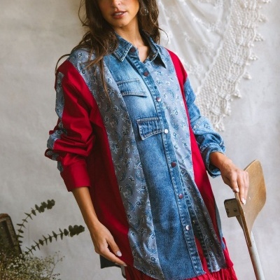 Camisa feminina patchwork azul, cinza e vermelho com botões, modelo junto a cadeira de madeira e planta.