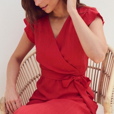Vestido vermelho com cinto e manga curta em mulher sentada em cadeira de madeira.