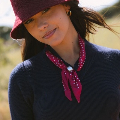 Mulher com chapéu vermelho, cachecol vermelho com bolinhas, camisola preta e brinco de argola.