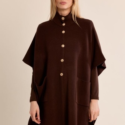 Mulher a usar poncho castanho escuro com botões dourados e bolso grande, com jeans azul