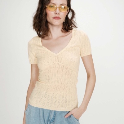 Mulher com camisola beige de malha, calças jeans azuis e óculos amarelos