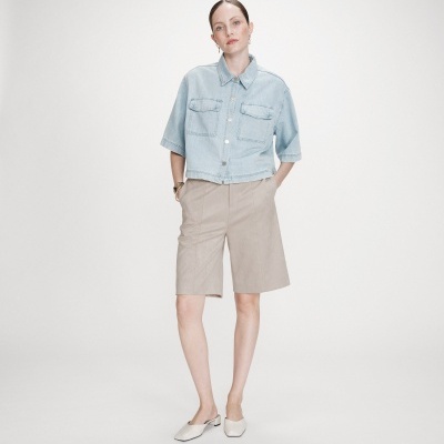 Mulher com camisola de ganga azul clara e calções bege em fundo branco