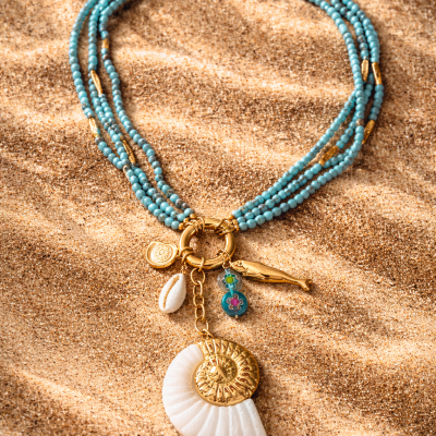 Colar com contas azuis e pendentes variados sobre areia
