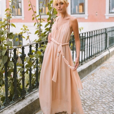 Vestido longo salmão com cinto de pérolas num cenário urbano com parapeito de ferro e calçada em pedra.