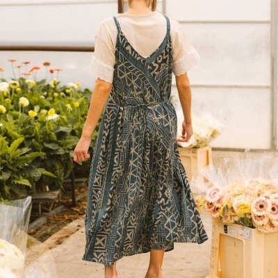 Vestido azul com padrão geométrico sobre t-shirt branca, sandálias castanhas, em estufa de flores