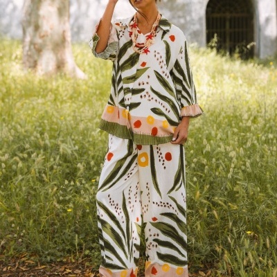 Conjunto feminino de calças largas e camisa estampada com padrão de folhas e círculos coloridos, usado com colar e sandálias