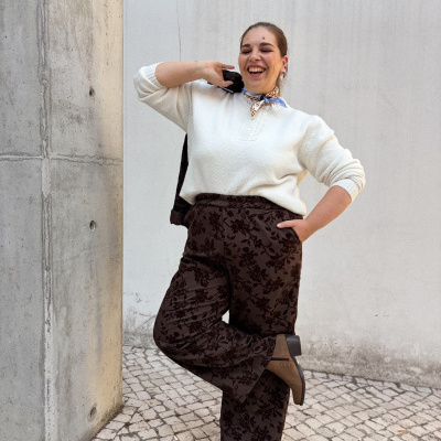 Mulher com camisola branca e calças castanhas com padrão floral