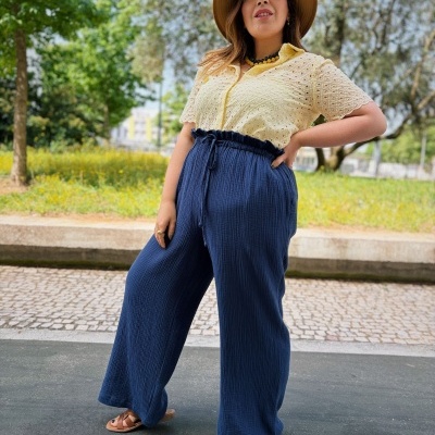 Mulher com blusa amarelo claro e calças largas azuis com chapéu castanho ao ar livre