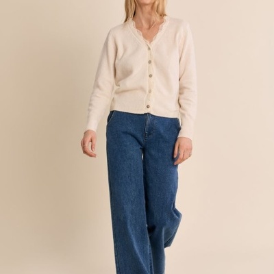 Pessoa com cardigan creme, calças de ganga largas azuis e sapatilhas claras num fundo bege
