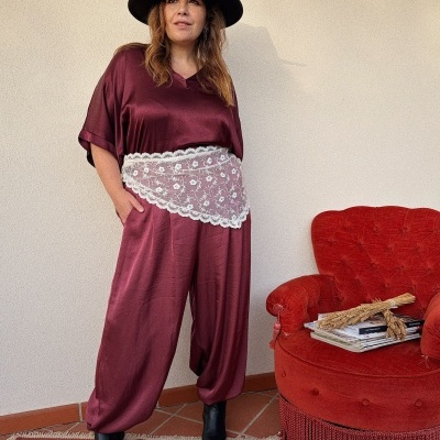 Mulher com macacão bordeaux e chapéu preto junto a poltrona vermelha.