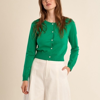 Mulher com cardigan verde e calções brancos em fundo bege