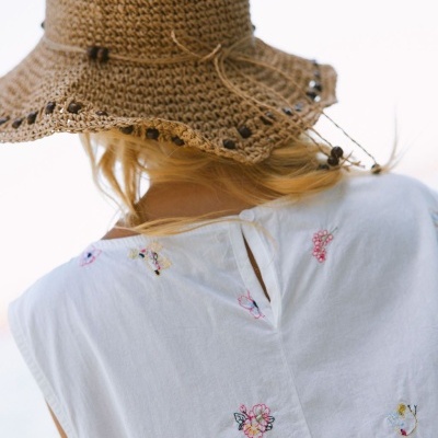 Chapéu de crochet castanho com contas e blusa branca com bordados de flores