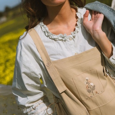 Mulher a usar blusa branca com folhos e macacão bege bordado