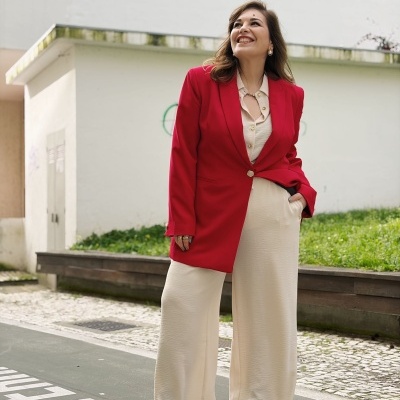 Mulher com blazer vermelho e calças largas creme ao ar livre
