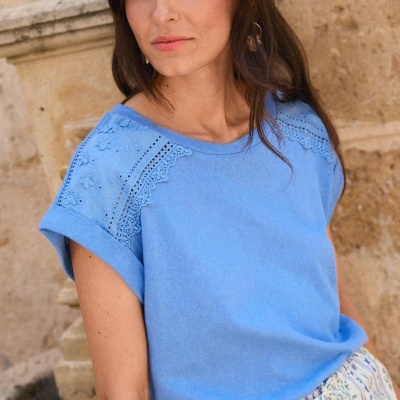 T-shirt azul clara com renda nas mangas e parede de pedra ao fundo