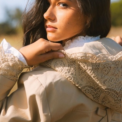 Mulher a usar trench coat bege com detalhes de renda e camisa branca com gola de renda