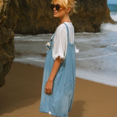 Vestido de ganga azul claro com bolso, t-shirt branca e óculos escuros na praia.