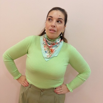 Mulher com camisola verde clara, lenço floral e calças largas bege
