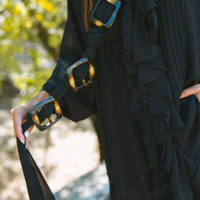 Cinto preto com três fivelas grandes de efeito tartaruga e vestido preto com folhos e pregas