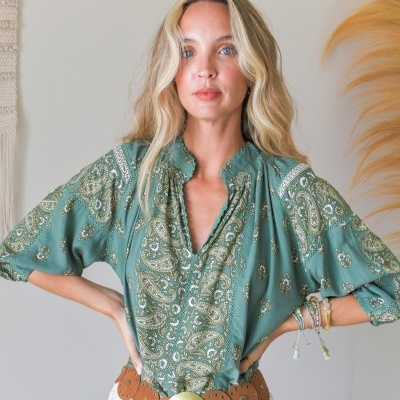 Mulher vestindo blusa verde com padrão paisley branco e verde e cinto castanho largo com fivela dourada