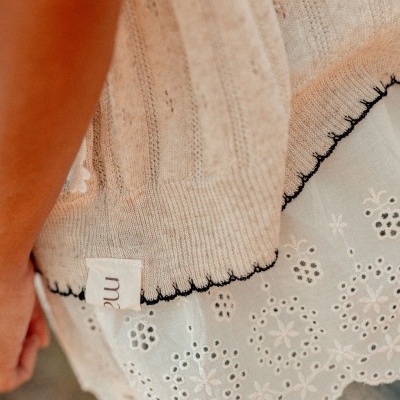 Peça de roupa feminina bege com bordado preto na bainha e tecido branco bordado floral