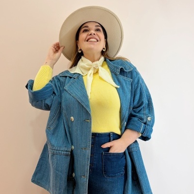 Mulher com casaco e calças de ganga, camisola amarela, lenço amarelo claro e chapéu bege de feltro