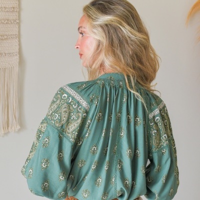 Blusa verde com padrão floral e detalhes de renda vista de costas.