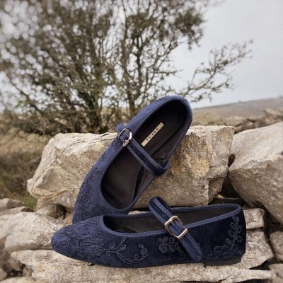 Sapatos Mary Jane azul escuro com padrão em relevo e fivela, sobre pedras em ambiente natural