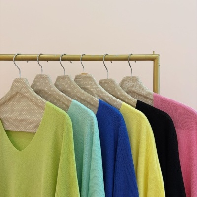 Seis camisolas coloridas de malha penduradas em cabides decorativos numa estrutura amarela