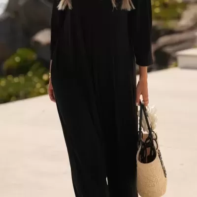 Vestido longo preto de manga três quartos com mala de palha clara e detalhe branco