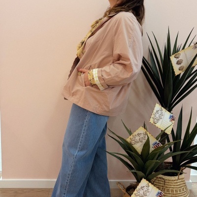 Mulher com blazer bege e jeans azuis perto de plantas em vasos trançados com postais