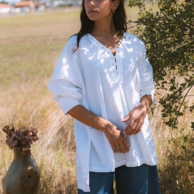 Mulher a usar blusa branca de algodão em ambiente natural com vegetação.