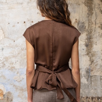Mulher de costas com blusa castanha de tecido acetinado e calças cinzentas com padrão xadrez