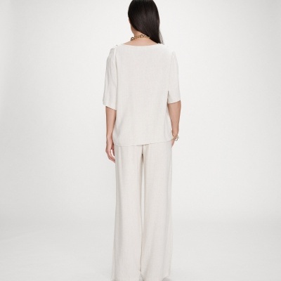 Mulher de costas com conjunto bege de blusa e calças largas em fundo branco