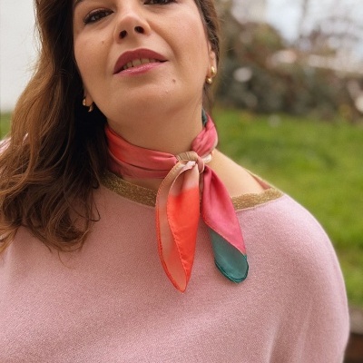 Mulher com cachecol colorido de tecido e camisola rosa com gola dourada.