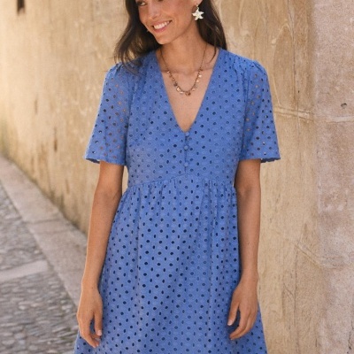 Vestido azul de algodão com bordado vazado usado por mulher junto a parede de pedra