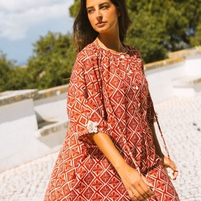 Vestido vermelho com padrão geométrico branco e botões brancos usado por mulher ao ar livre
