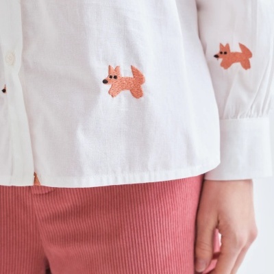 Camisa branca com bordados de raposas e calças rosas.
