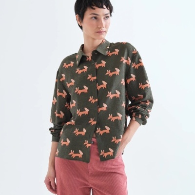 Mulher com camisa verde estampada de raposas cor de rosa e calças cor-de-rosa de veludo cotelê.