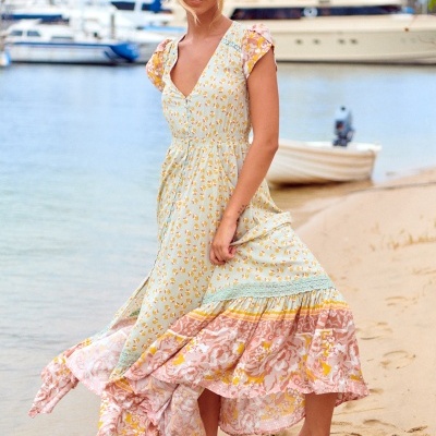 Mulher com vestido longo floral numa praia com barcos ao fundo
