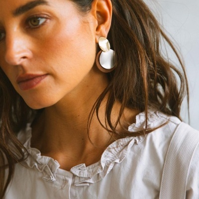 Brincos grandes dourados, prateados e castanhos usados por mulher com blusa branca