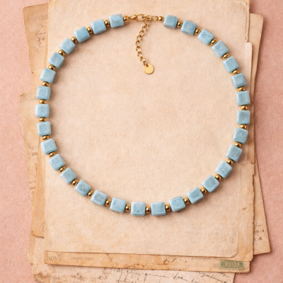 Colar com contas quadradas azuis e douradas sobre papéis envelhecidos
