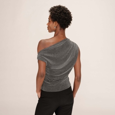 Mulher de costas com blusa cinzenta assimétrica e calças pretas.