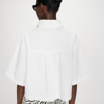 Camisa branca de manga curta vista de costas numa modelo com calças de padrão zebra.