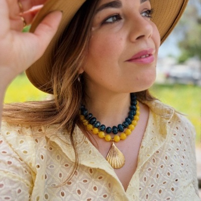 Mulher com chapéu bege, colar duplo com contas amarelas e negras e pendente dourado, camisa amarela de algodão bordado.