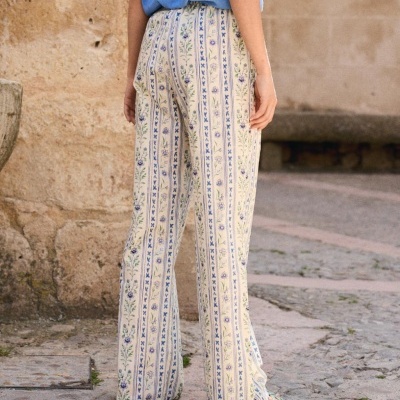 Calças compridas creme com padrão floral e listras azuis e t-shirt azul clara em cenário exterior de pedra.