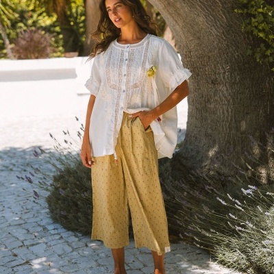 Mulher vestindo blusa branca com rendas e calças culotte amarelas com padrão floral ao ar livre
