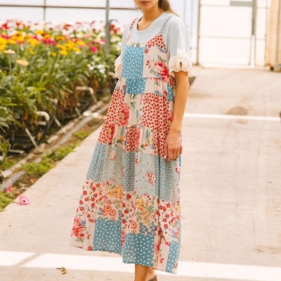 Mulher com vestido patchwork florido e t-shirt branca numa estufa com flores.